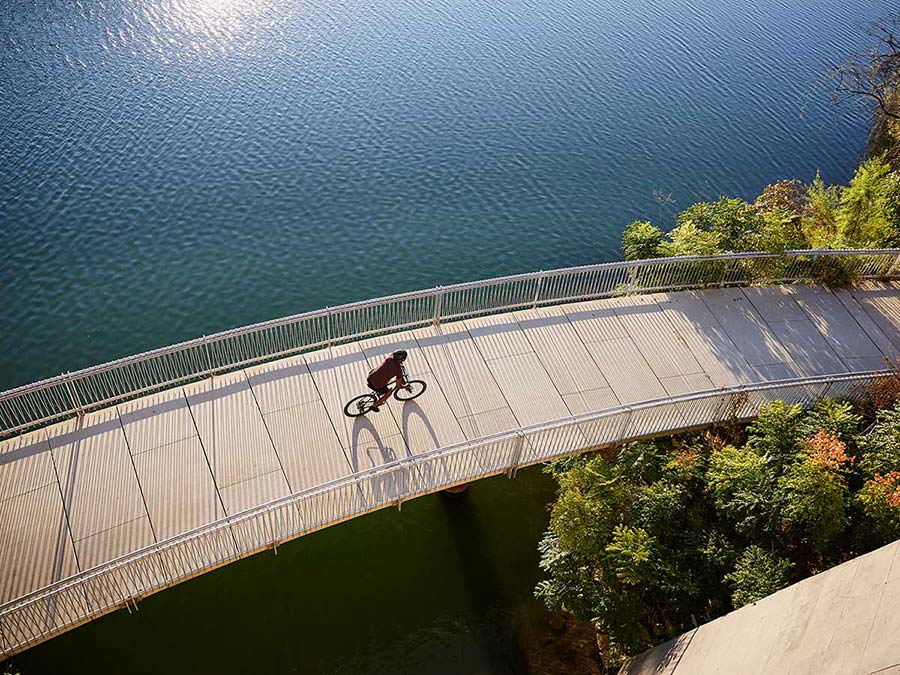 Cyclist wearing helmet while riding bike across bridge over body of water