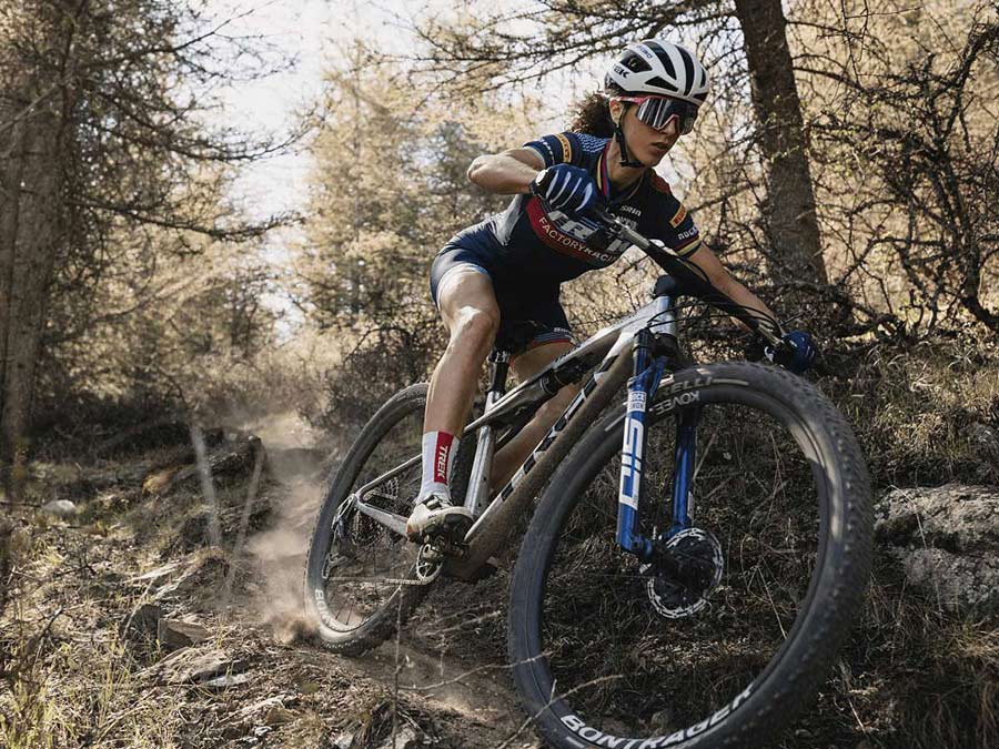 Cyclist wearing helmet and sunglasses while riding bike on dirt trail with trees in background