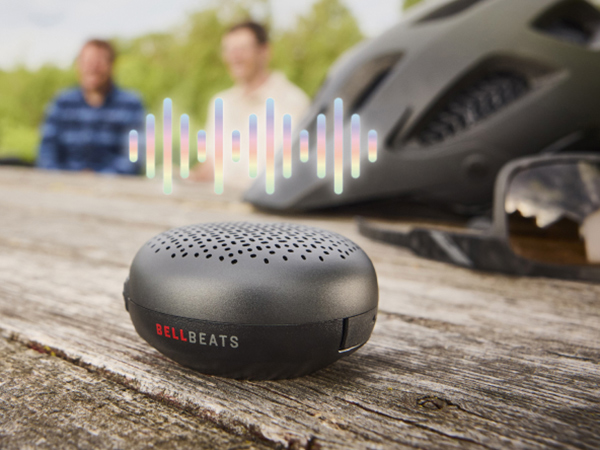 Illustration of sound wave above BellBeats while sitting on table with people, helmet and sunglasses in background