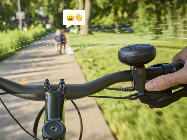 Bike on paved path while BellBeats mounted to handlebar with emojis in speak bubbles above people in background