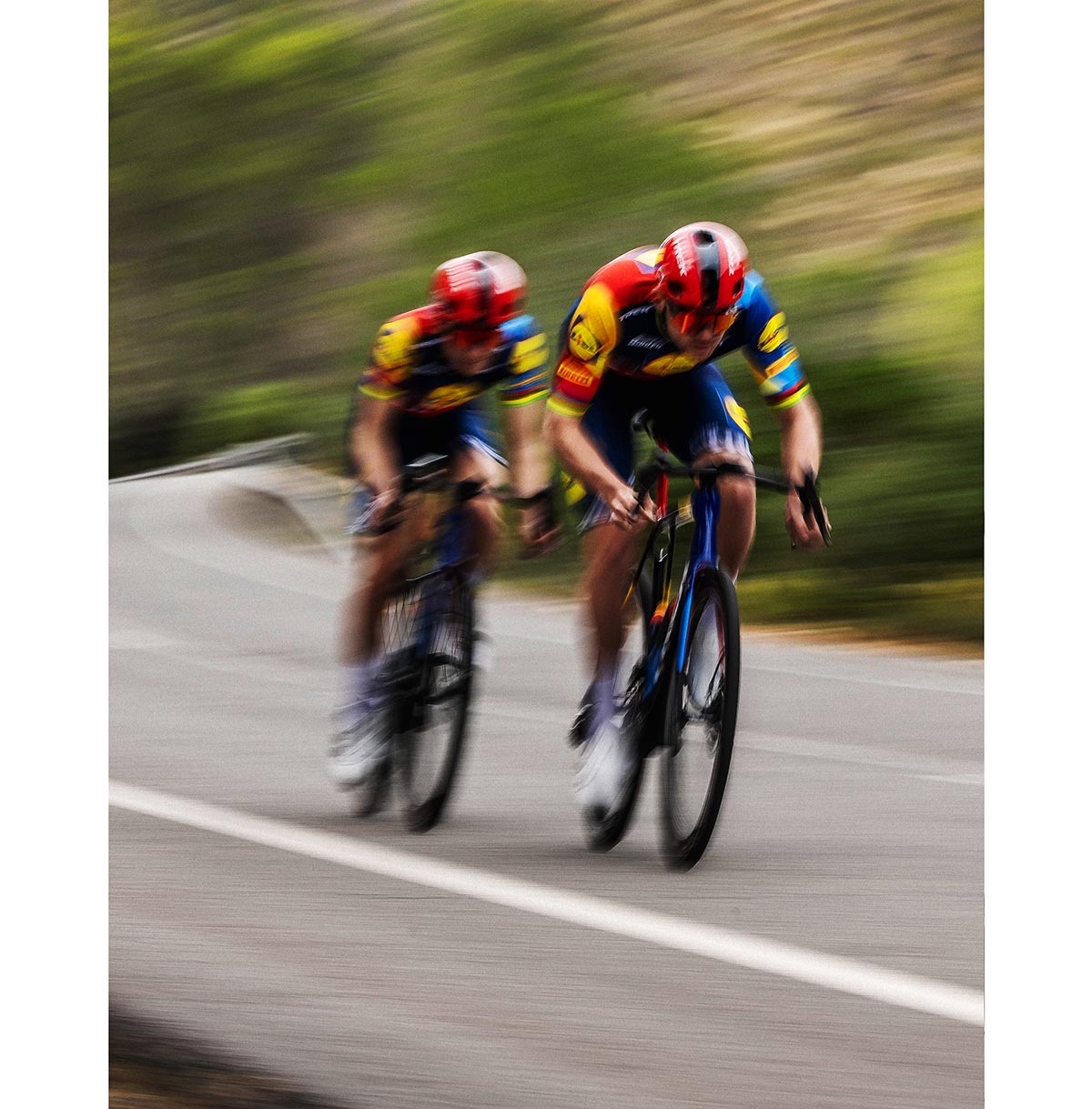 Blurred image of Trek-Lidl riders wearing helmet and team gear while riding bikes on a tarmac road