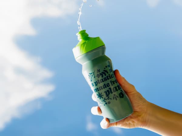 Trek's new recycled plastic water bottle, being held up to a bright blue sky with clouds